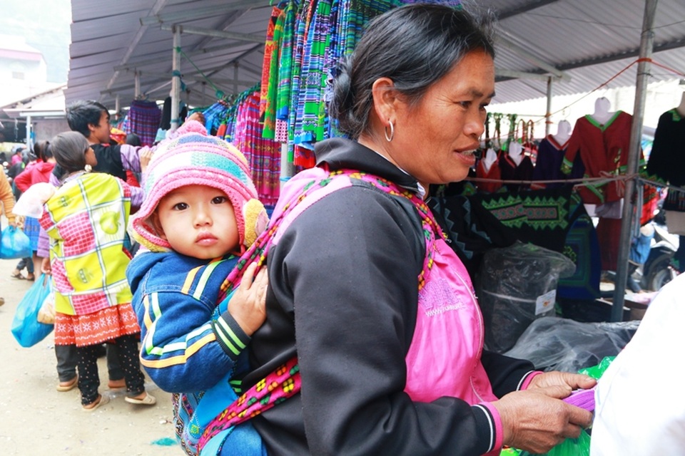 Nhiều phụ nữ đến chợ từ rất sớm, địu theo cả con nhỏ sau lưng. Ánh mắt của đứa trẻ ngơ ngác vì lần đầu tiên trong đời được đi chợ - nơi có nhiều người nhộn nhịp mua bán, trao đổi hàng hóa.