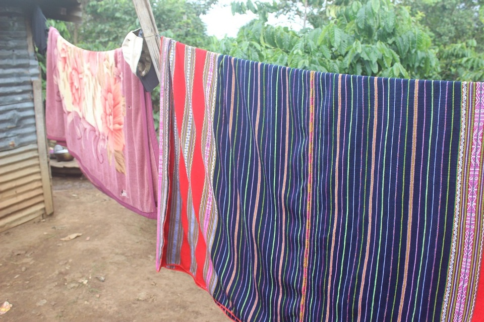 Tranh thu trời nắng, bà H’Bơi mang chiếc chăn thổ cẩm ra phơi