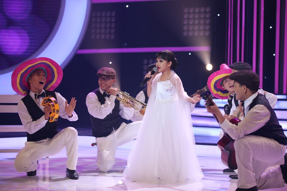 Hoài Linh “đe dọa” Xuân Bắc vì chê giọng hát địa phương khó nghe - 8 “Út cưng” của chương trình xuất hiện lộng lẫy với chiếc váy cưới trắng tinh khôi, mái tóc búi cài hoa và cách trang điểm được đánh giá “siêu” giống với phiên bản gốc. Từng cử điệu xoay vòng, liếc mắt duyên dáng và thần thái trên khuôn mặt của bé khiến cả khán phòng liên tục dành tặng những tràng pháo tay hòa theo giai điệu vui nhộn của bài hát.