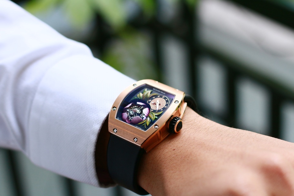 Sắp khai mạc triển lãm SIHH 2017 – Cuộc chơi của các ông lớn ngành đồng hồ Thụy Sỹ - 3 Cận cảnh siêu phẩm Richard Mille RM19-02 Tourbillon Fleur trên cổ tay chủ nhân tại Hà Nội, một trong số 30 siêu phẩm trị giá hơn triệu đô của dòng RM 19-02 còn sót lại trên toàn thế giới. RM19-02 đặc biệt ở chỗ cỗ Tourbillon hoàn toàn được giấu kín trong bông Mộc Lan tím. Cứ mỗi 5 phút, các cánh hoa hé nở mới khoe trọn cỗ máy đắt giá này cũng như phần nhuỵ hoa bằng đá quý. Để tạo ra chuyển động quyến rũ như vậy, RM 19-02 Tourbillon Fleur đòi hỏi một cơ chế phức tạp với 5 cần gạt bên dưới và các bánh răng chuyền dài để nâng cỗ “flying tourbillon” lên mỗi khi bông hoa nở ra.