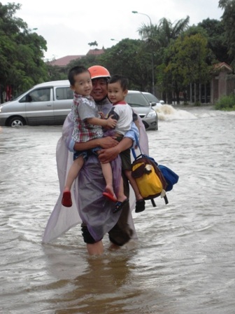 Hai phụ huynh loay hoay mặc áo mưa cho con giữa biển nước mênh mông