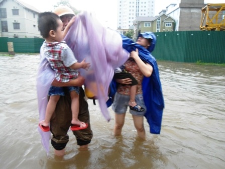 Hai phụ huynh loay hoay mặc áo mưa cho con giữa biển nước mênh mông