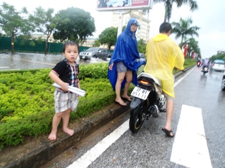 Cháu bé ướt sũng, ngoan ngoãn đứng chờ bố mẹ sửa xe.