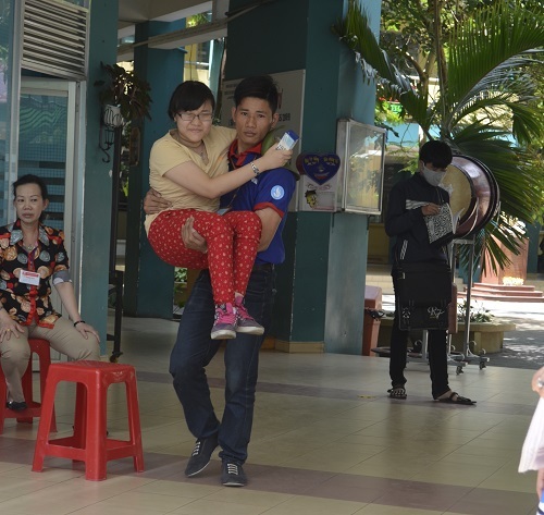 Thí sinh đi xe lăn hoàn thành kỳ thi THPT quốc gia - 1 Sinh viên tình nguyện hỗ trợ bế Thanh Vy lên và xuống phòng thi. (Ảnh: Tuấn Cường)