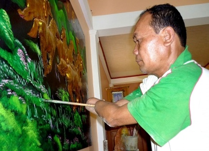Thầy giáo cụt tay mê vẽ và chuyện tình cổ tích - 2 Thầy Khanh Rông họa thêm chi tiết cho bức tranh sơn dầu mừng nhà mới. (Ảnh: Báo Cà Mau)